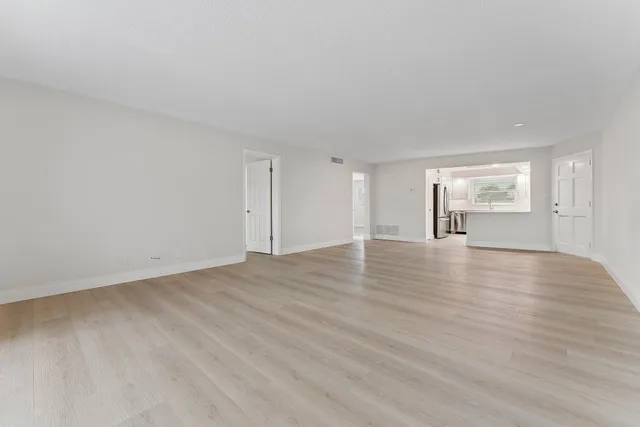 a view of empty room with wooden floor and kitchen