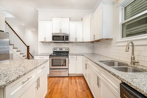 a kitchen with granite countertop a sink a stove top oven and cabinetry