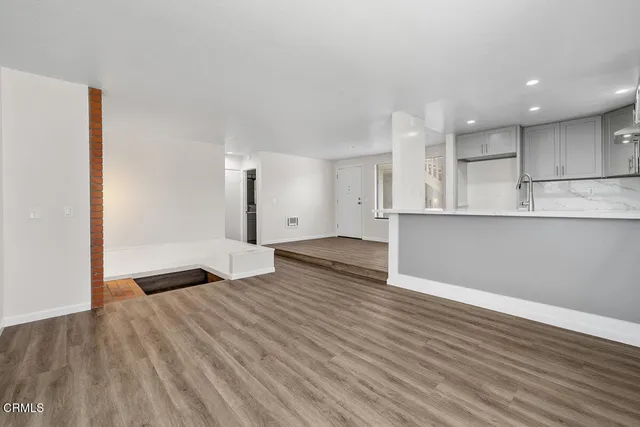 a view of an empty room with wooden floor and a kitchen