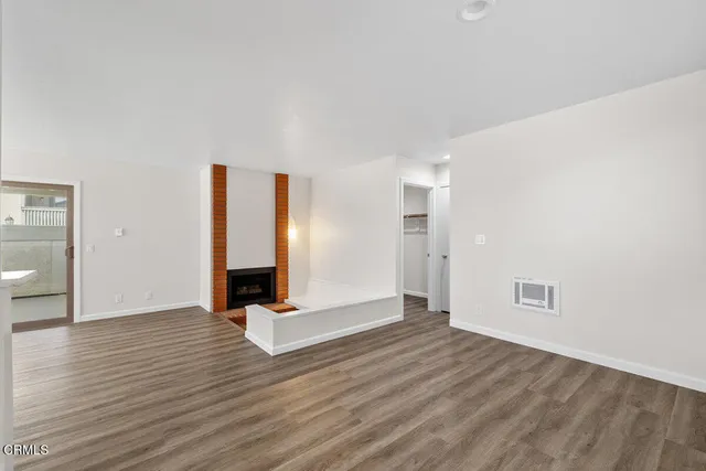 a view of an empty room with wooden floor and fireplace