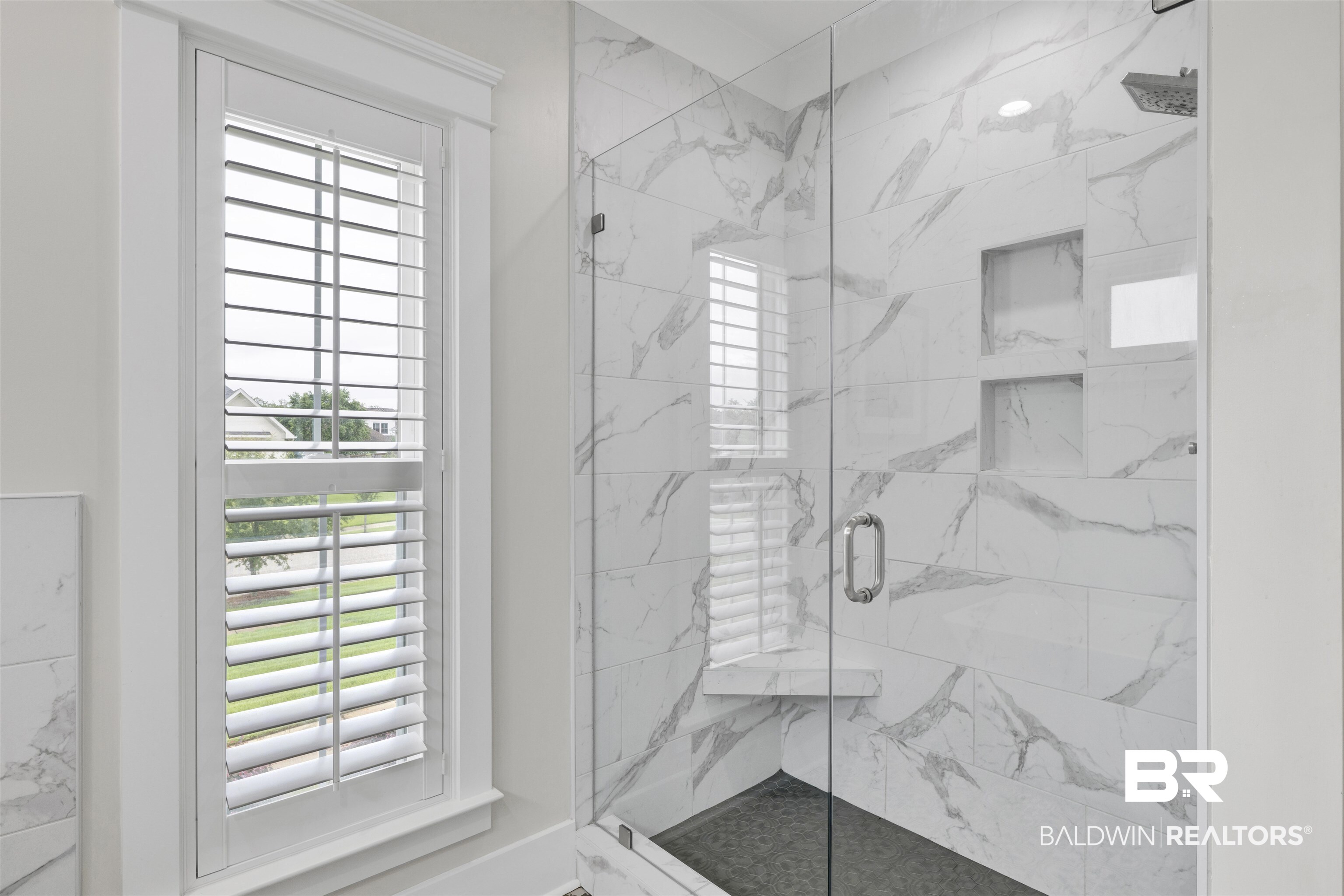 21702 Pillars Street Fairhope, AL 36532 - Photo 25 of 54 Walk-in shower featuring a glass enclosure, large format marble-look tile, built-in recessed shelving, a corner bench, and a dark tile shower pan