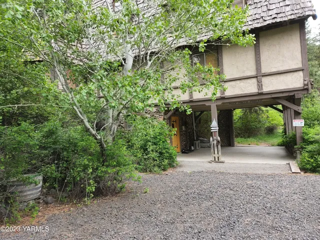 a backyard of a house with large trees and a wooden bench