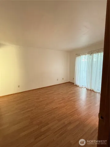 an empty room with wooden floor and windows with curtains