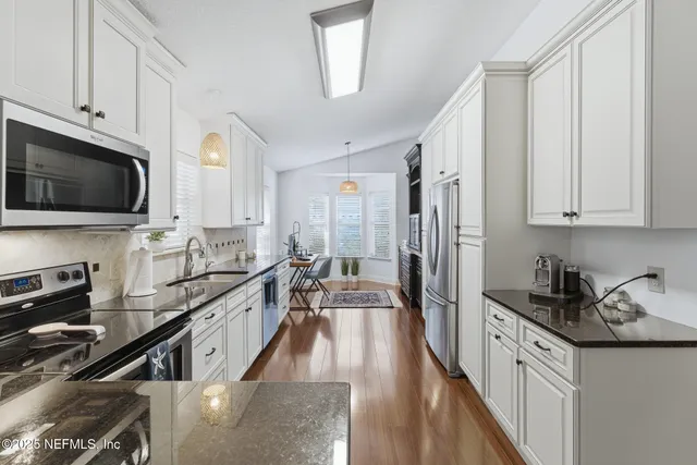 a kitchen with stainless steel appliances granite countertop a stove top oven a sink a dining table and chairs with wooden floor