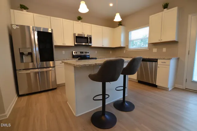 a kitchen with granite countertop a refrigerator a stove a sink cabinets and wooden floor