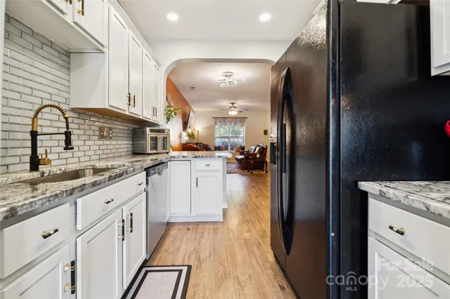 a kitchen with stainless steel appliances granite countertop a refrigerator a sink and white cabinets