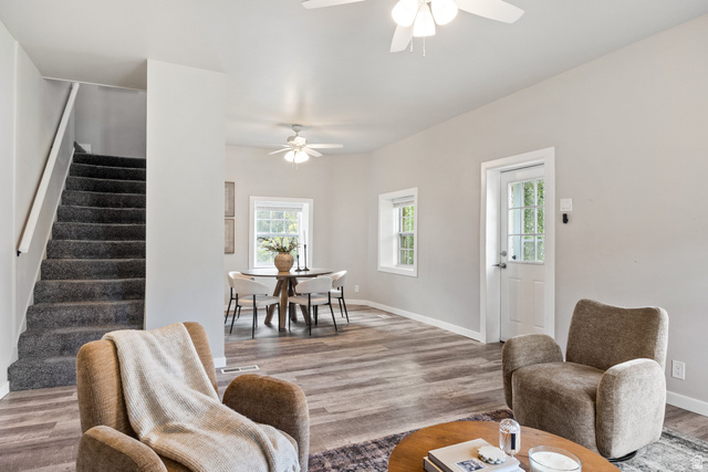 Wood-finish flooring, staircase with carpeted treads, ceiling fans, and multiple windows with white trim