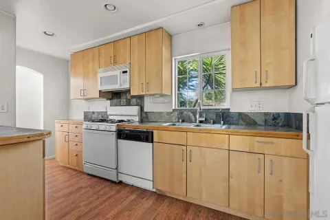 a kitchen with stainless steel appliances granite countertop a refrigerator a sink dishwasher a s stove top oven a dining table and chairs with wooden floor