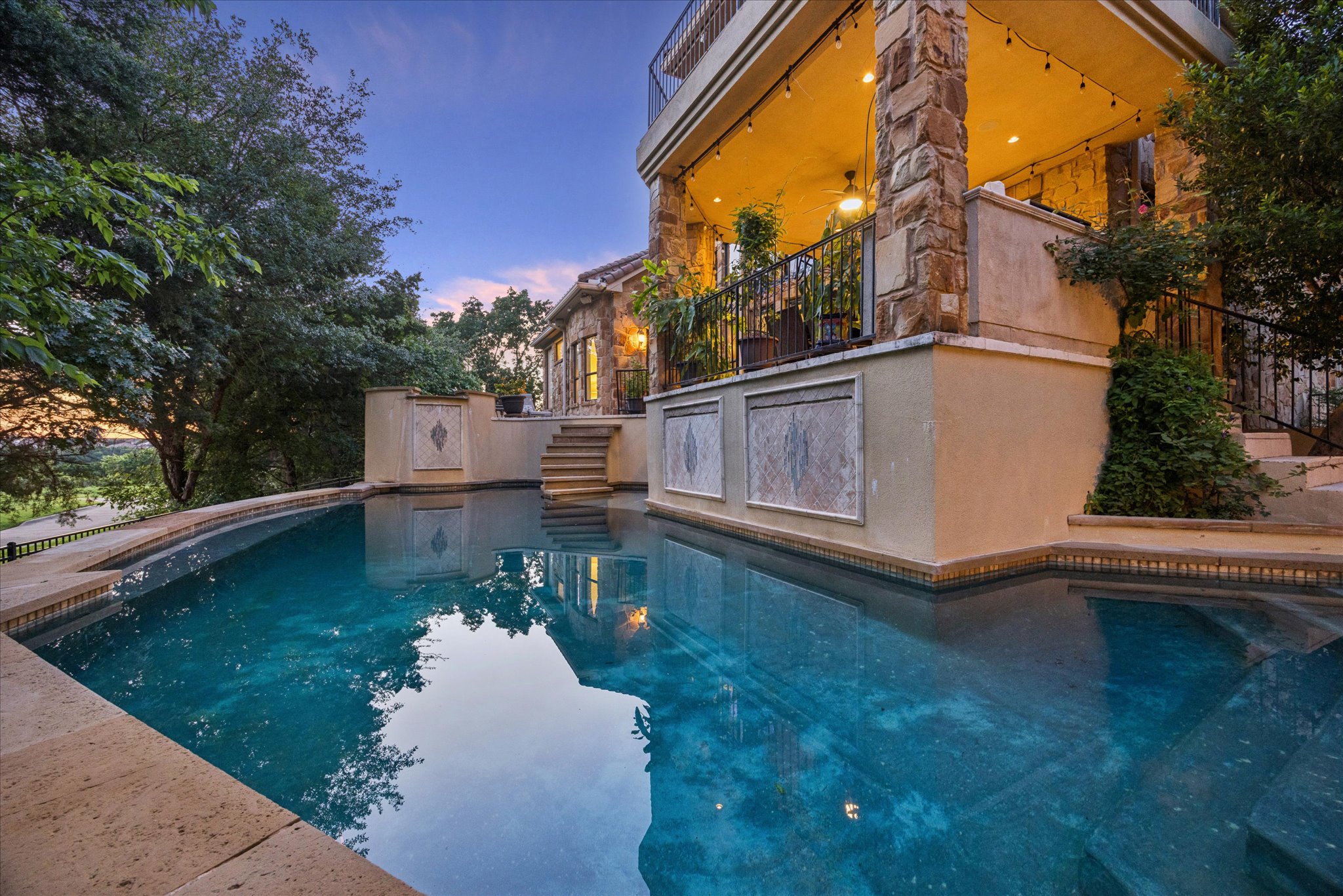 11805 Ranchview Court Austin, TX 78732 - Photo 30 of 36 Curved swimming pool with stone coping, featuring a multi-level patio with stone pillars, an upper-level balcony, and exterior lighting