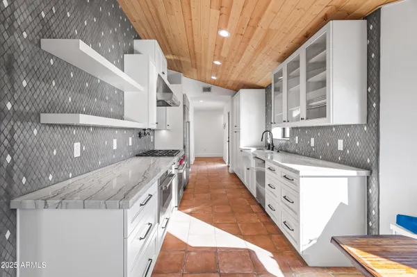 a large white kitchen with granite countertop a sink and dishwasher a stove top oven with wooden floor