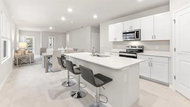 a kitchen with stainless steel appliances a sink a stove a refrigerator cabinets and chairs