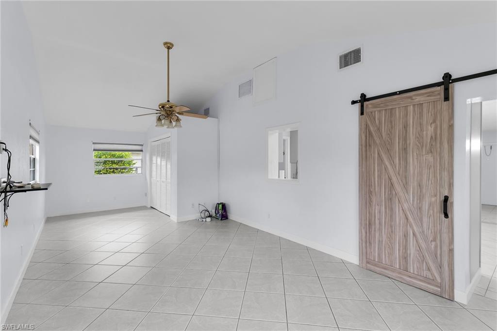 4502 22nd Place Southwest Naples, FL 34116 - Photo 13 of 30 Unfurnished living room with high vaulted ceiling, a ceiling fan, a barn door, and light tile patterned floors