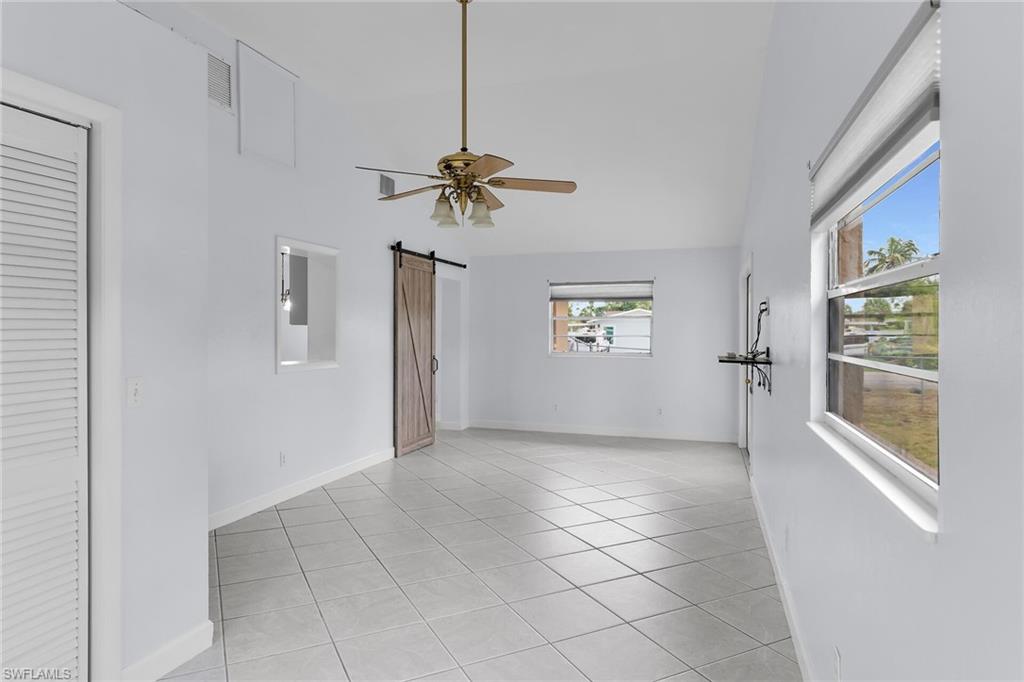 4502 22nd Place Southwest Naples, FL 34116 - Photo 15 of 30 Unfurnished room featuring a barn door, light tile patterned flooring, ceiling fan, and high vaulted ceiling