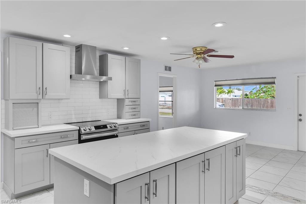 4502 22nd Place Southwest Naples, FL 34116 - Photo 23 of 30 Kitchen with wall chimney range hood, electric stove, a kitchen island, backsplash, and recessed lighting