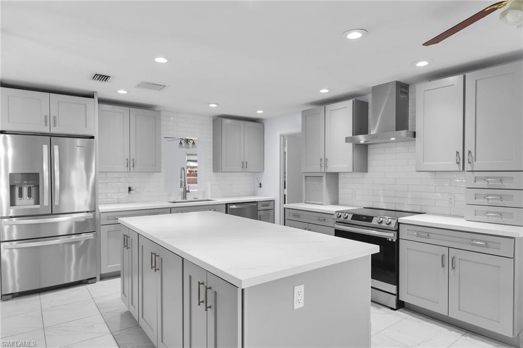 4502 22nd Place Southwest Naples, FL 34116 - Photo 7 of 30 Kitchen with stainless steel appliances, a ceiling fan, gray cabinets, wall chimney exhaust hood, and light marble finish flooring