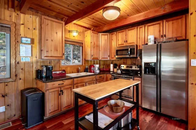 a kitchen with stainless steel appliances granite countertop a refrigerator a stove a sink a dining table and chairs with wooden floor