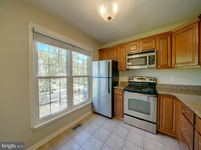 a kitchen with stainless steel appliances granite countertop a refrigerator oven a sink dishwasher and wooden cabinets with a large window