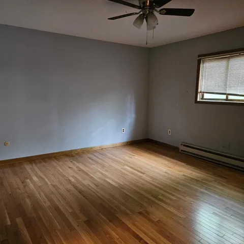 an empty room with wooden floor fan and windows