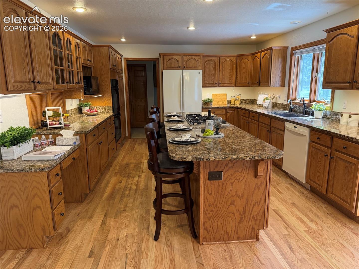 15430 Bar X Road Colorado Springs, CO 80908 - Photo 19 of 50 The gourmet island kitchen showcases hardwood floors, rich wood cabinetry, granite countertops, a planning desk, dining nook, and access to an expansive composite deck.