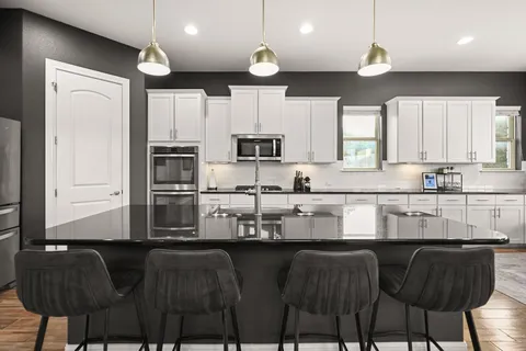 a kitchen with stainless steel appliances granite countertop a stove top oven a sink a refrigerator and white cabinets