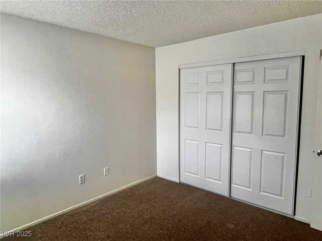 5304 Harmony Street, Unit HOME Las Vegas, NV 89107 - Photo 13 of 17 Unfurnished bedroom with dark carpet, a textured ceiling, and a closet