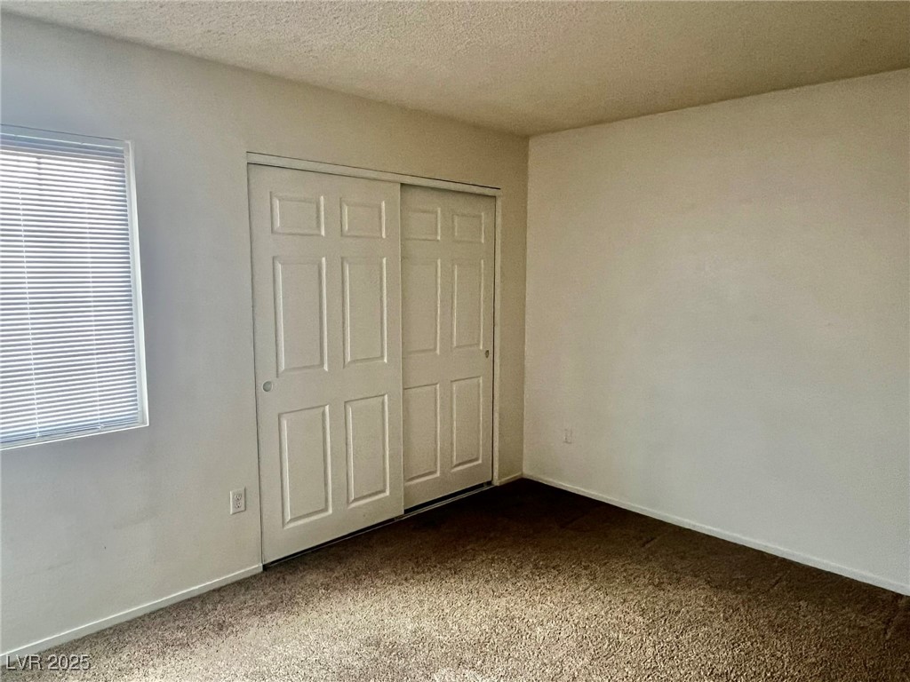 5304 Harmony Street, Unit HOME Las Vegas, NV 89107 - Photo 15 of 17 Unfurnished bedroom featuring dark carpet, a closet, a textured ceiling, and multiple windows