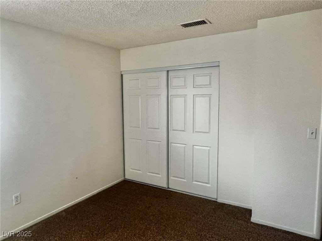 5304 Harmony Street, Unit HOME Las Vegas, NV 89107 - Photo 17 of 17 Unfurnished bedroom featuring dark colored carpet, a textured ceiling, and a closet