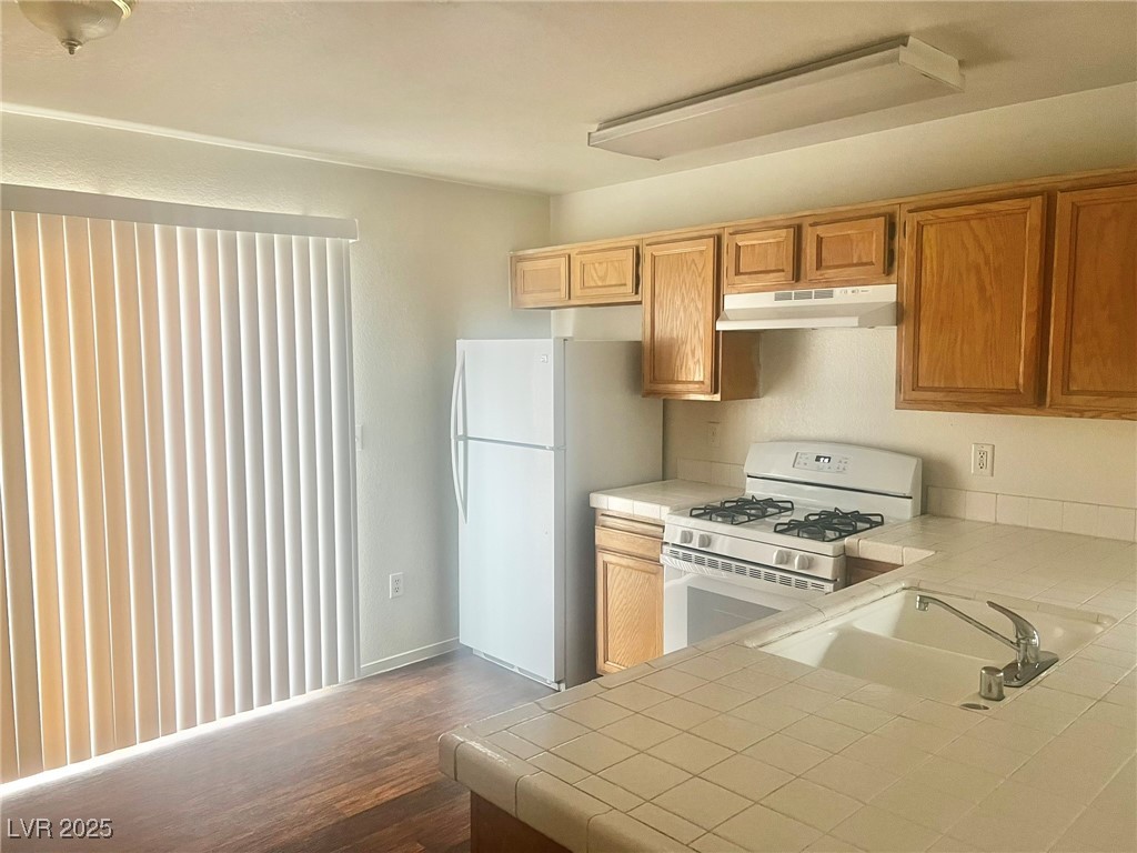 5304 Harmony Street, Unit HOME Las Vegas, NV 89107 - Photo 5 of 17 Kitchen featuring white appliances, tile countertops, under cabinet range hood, and dark wood-style flooring
