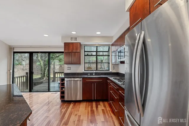 a kitchen with stainless steel appliances granite countertop a refrigerator a sink dishwasher a stove and white countertops with wooden floor