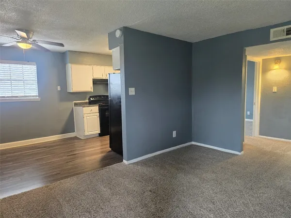 a view of empty room with wooden floor and kitchen