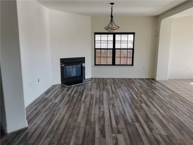 a view of an empty room with wooden floor fireplace and a window