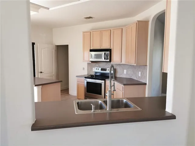 a kitchen with kitchen island granite countertop a refrigerator a stove a sink and white cabinets