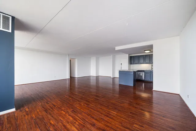 a view of empty room with wooden floor and kitchen