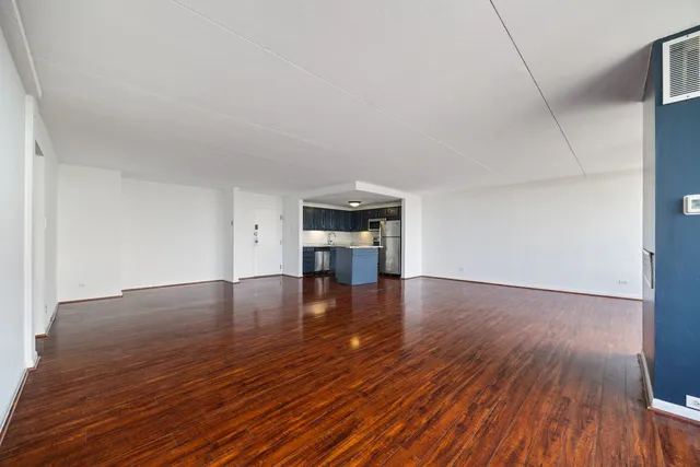 a view of empty room with wooden floor and kitchen