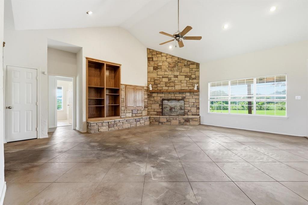 12190 Bell Road Pilot Point, TX 76258 - Photo 9 of 39 Living area featuring a stone-clad fireplace with wood mantel, vaulted ceiling with recessed lighting and ceiling fan, and large windows