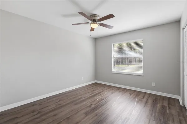 an empty room with wooden floor fan and windows