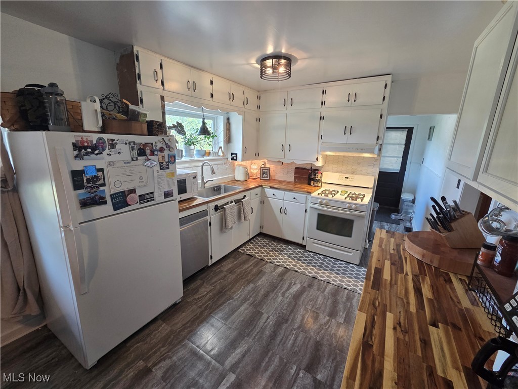 Kitchen with white appliances, white cabinets, butcher block counters, backsplash, and under cabinet range hood