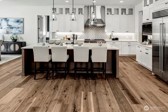 a large kitchen with stainless steel appliances kitchen island granite countertop a large stove a refrigerator a sink dishwasher and white cabinets with wooden floor