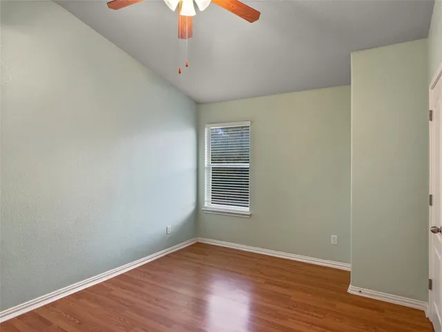 a view of an empty room with wooden floor fan and window