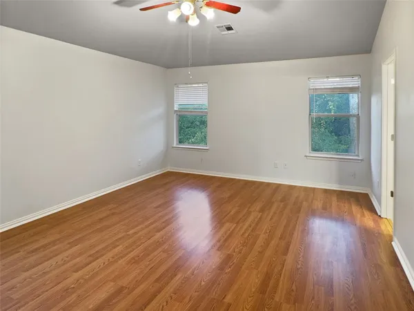 an empty room with wooden floor chandelier fan and windows