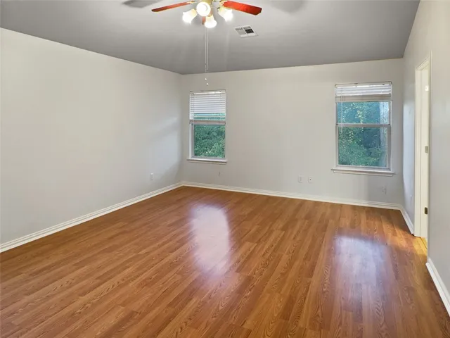 an empty room with wooden floor chandelier fan and windows