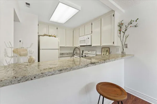 a kitchen with stainless steel appliances granite countertop a sink a stove a refrigerator white cabinets and wooden floor