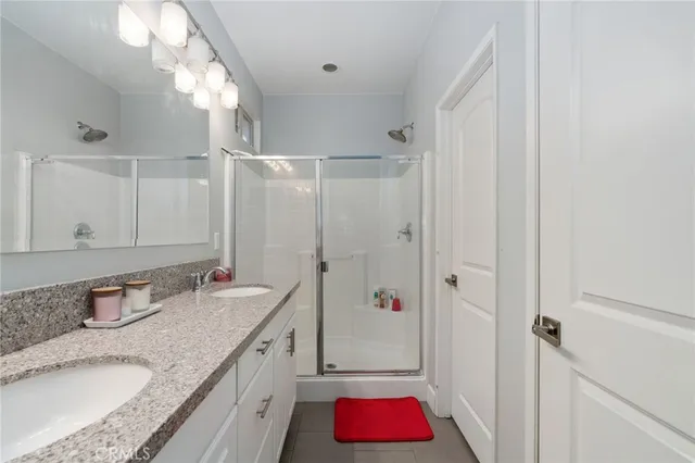 a bathroom with a granite countertop double vanity sink and shower