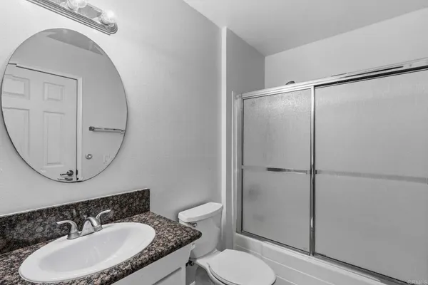 a bathroom with a granite countertop sink toilet mirror and a shower