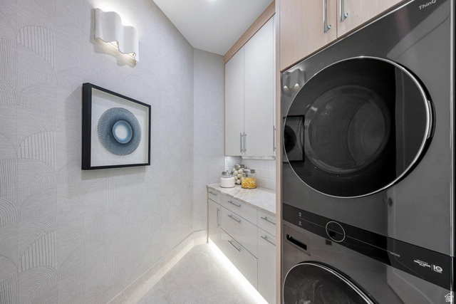 2867 East Granite Way St. George, UT 84790 - Photo 51 of 69 Integrated laundry area featuring a stacked washer and dryer, under-cabinet lighting, contemporary wall sconce, upper and lower cabinetry, and a light-toned countertop