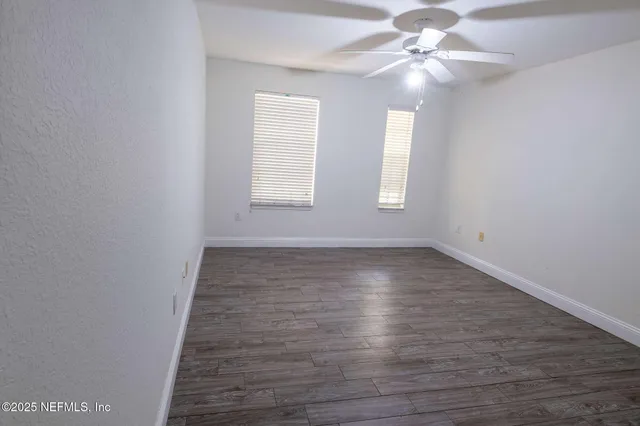 an empty room with wooden floor fan and windows