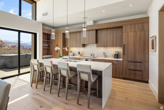 214 Lionsback Loop, Unit 37 Moab, UT 84532 - Photo 6 of 21 Modern kitchen featuring light wood-finish flooring, a large center island with seating, dark wood-finish cabinetry, built-in panel-ready appliances, and a full wall of glass sliding doors opening to a patio with a distant mountain backdrop