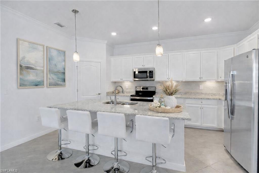 17609 Ashcomb Way Estero, FL 33928 - Photo 4 of 40 Kitchen with stainless steel appliances, white cabinets, backsplash, and ornamental molding