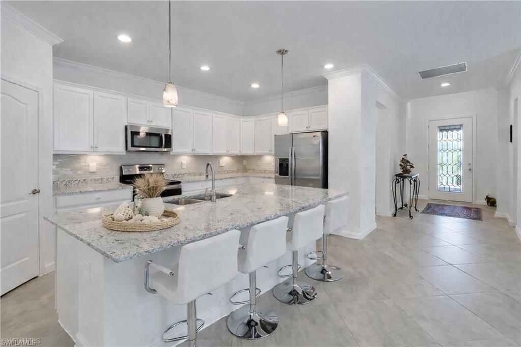 17609 Ashcomb Way Estero, FL 33928 - Photo 7 of 40 Kitchen featuring white cabinetry, stainless steel appliances, light stone countertops, decorative backsplash, and crown molding