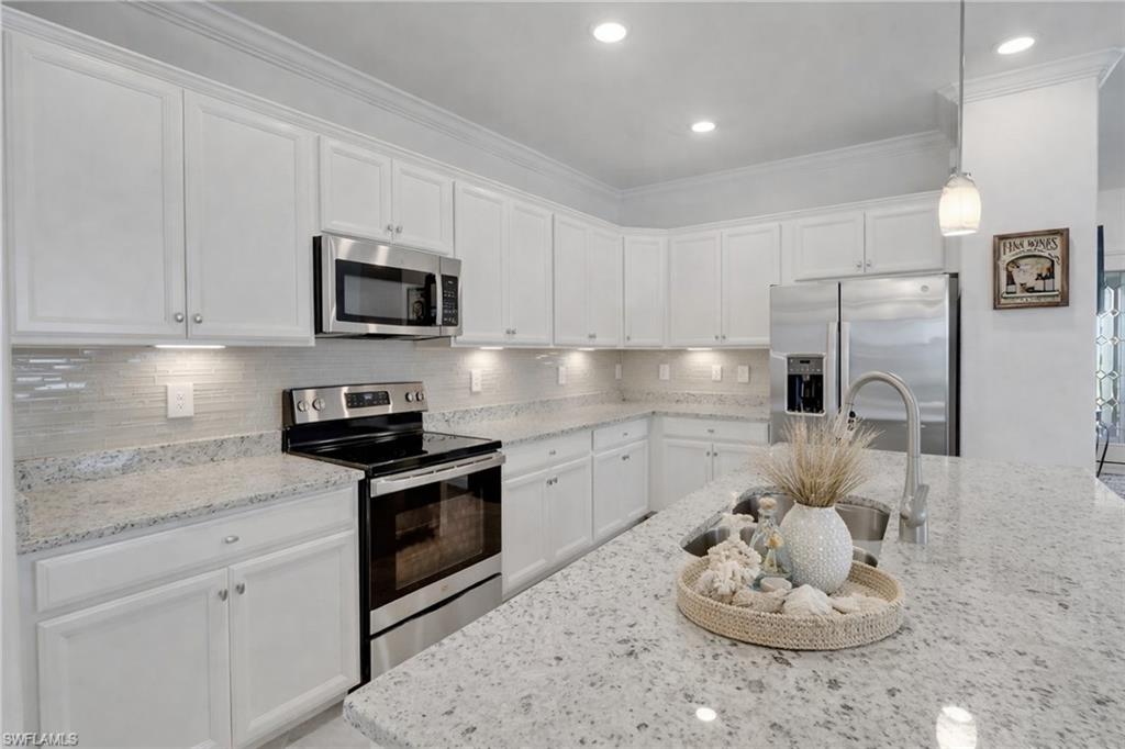 17609 Ashcomb Way Estero, FL 33928 - Photo 8 of 40 Kitchen with stainless steel appliances, white cabinetry, decorative backsplash, hanging light fixtures, and light stone counters